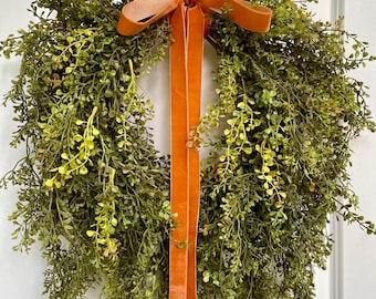 May include: A green leafy wreath with a long orange velvet ribbon tied in a bow.