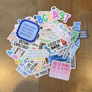 K&ouml;nnte beinhalten: Eine Sammlung bunter Aufkleber mit verschiedenen Texten und Designs. Die Aufkleber zeigen S&auml;tze wie "Fade your prompts not your patience" und "Celebrate tiny victories". Die Aufkleber liegen auf einer Holzoberfl&auml;che.
