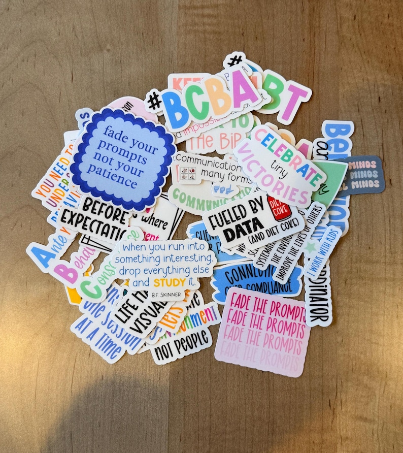 K&ouml;nnte beinhalten: Eine Sammlung bunter Aufkleber mit verschiedenen Texten und Designs. Die Aufkleber zeigen S&auml;tze wie "Fade your prompts not your patience" und "Celebrate tiny victories". Die Aufkleber liegen auf einer Holzoberfl&auml;che.