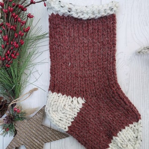 Peut inclure: Une chaussette de Noël en tricot rouge et blanche. La chaussette a un revers blanc et un bout blanc.