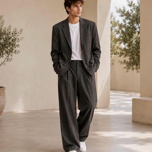 May include: A charcoal grey suit consisting of a single-breasted blazer with notched lapels and matching wide-leg trousers with a pleated front, worn over a plain white crew-neck t-shirt and paired with simple white trainers.