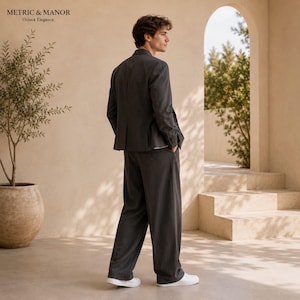 May include: A dark grey blazer and matching wide-leg trousers worn with white trainers. The text "METRIC & MANOR" and "Unlock Elegance." appears in the upper left corner. The outfit features a structured jacket and loose-fitting trousers.
