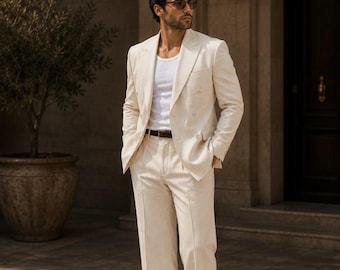 May include: A cream-colored suit with a double-breasted jacket and matching trousers. The outfit includes a white undershirt, a brown leather belt, and brown and white dress shoes. The image also features the text "METRIC & MANOR UNLOCK ELEGANCE."