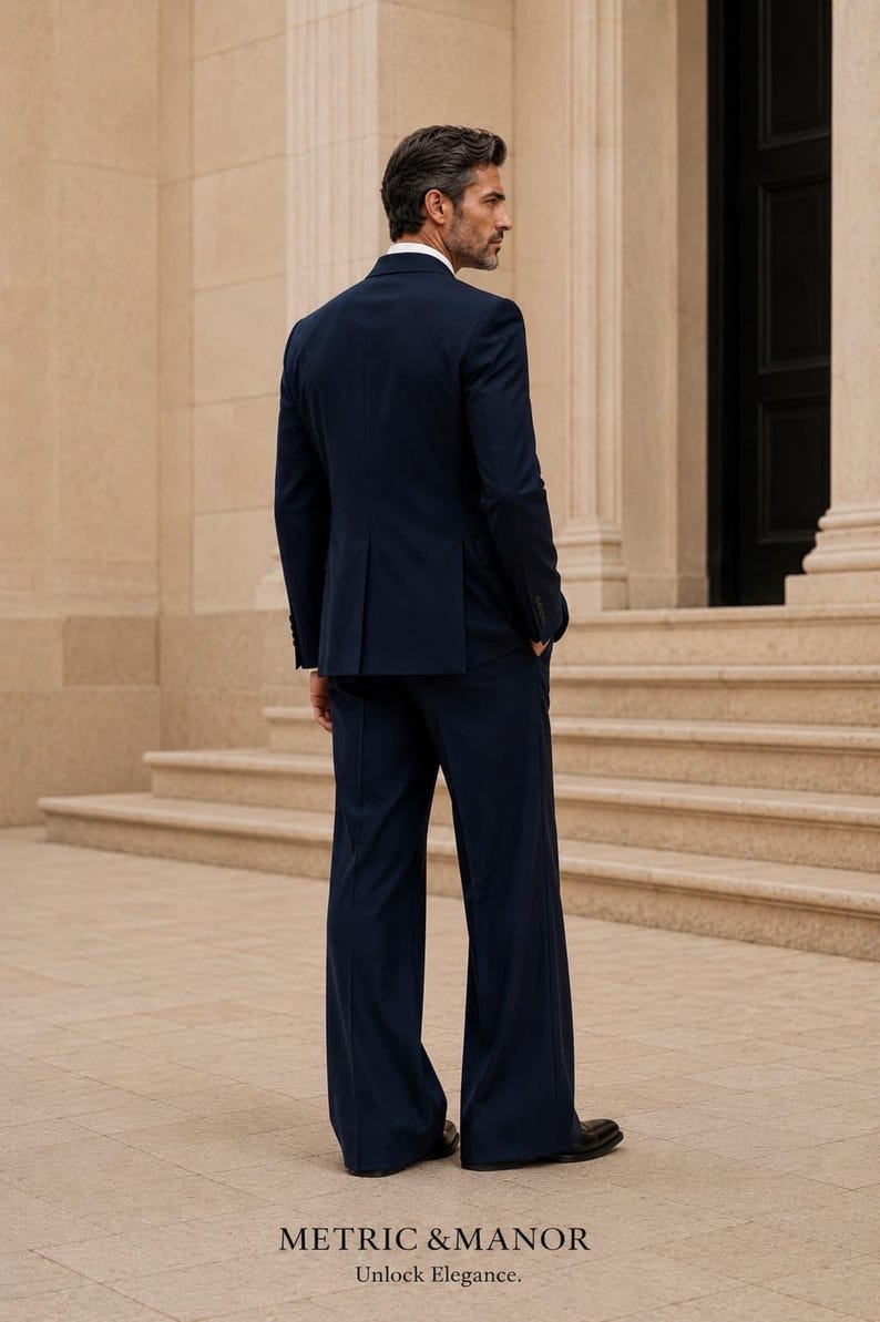 May include: A dark navy blue suit consisting of a tailored blazer and matching wide-leg trousers. The text at the bottom reads METRIC & MANOR Unlock Elegance. The suit features a structured back with a center vent and long sleeves.