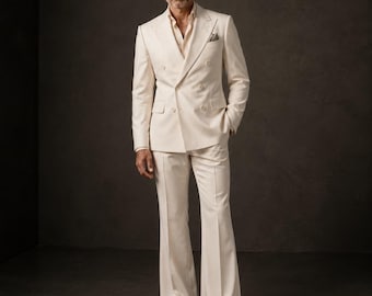 May include: A cream-colored double-breasted suit featuring a blazer with wide peak lapels and a pocket square, paired with matching flared trousers and a light beige button-down shirt. The text "METRIC & MANOR Unlock Elegance." appears at the bottom.