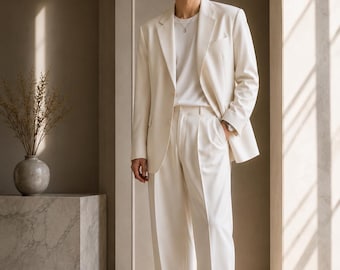 May include: Cream-colored suit consisting of a blazer, trousers, and a white t-shirt. The blazer has a notched lapel and a pocket. The trousers are pleated. The outfit is paired with white sneakers. The text "METRIC & MANOR" is at the top.