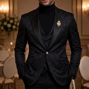 May include: A black blazer with a subtle floral jacquard pattern, featuring satin lapels, a single gold button closure, and a gold crest pin on the left lapel. The blazer is worn over a black turtleneck sweater and a matching black vest.