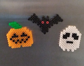 May include: Three Halloween-themed bead crafts: a pumpkin with a black face, a black bat with red eyes, and a white ghost with a black face.