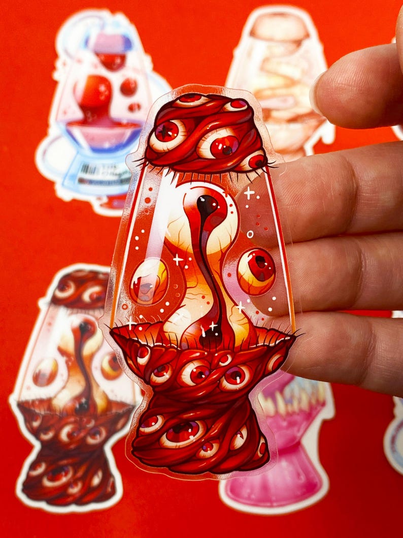 Pu&ograve; includere: Un adesivo trasparente con un design stilizzato di una lampada a lava nei toni del rosso e dell'arancione. La lampada &egrave; decorata con numerosi occhi rossi e una struttura centrale a forma di occhio. Altri adesivi sono visibili sullo sfondo.