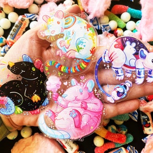 May include: Four colorful rat stickers with rainbow, galaxy, and cotton candy designs. The stickers are on a hand with a tattoo and a background of colorful candy.