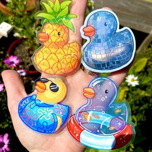 May include: Four quirky duck stickers. One is a pineapple, another a disco ball, a third wearing sunglasses and a patterned shirt, and the last one is inside a pool float with fish.