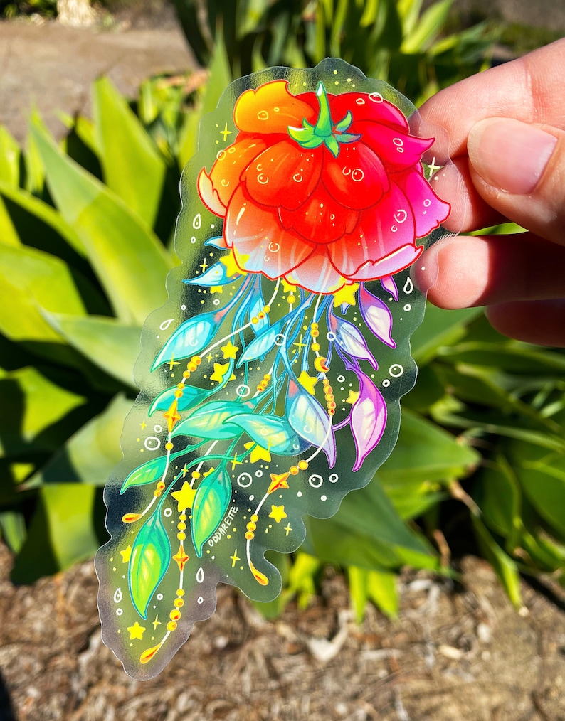Puede incluir: Una pegatina transparente con una flor roja, naranja y rosa con hojas verdes y estrellas amarillas. La pegatina tiene el texto "ODDFIRE".