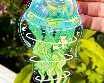 May include: A clear sticker with a green and blue alien spaceship inside a green jellyfish. The spaceship has a dome and contains a small cow, a fish, and a green alien. The jellyfish has a swirling pattern and is surrounded by a white background.