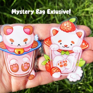 May include: Two clear stickers featuring cartoon illustrations of adorable white cats with pink accents. The cats are depicted in a glass of pink milk with a strawberry on top. The stickers are labeled "Mystery Bag Exclusive!"