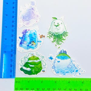 May include: A collection of five whimsical stickers featuring aquatic and natural themes. Designs include a jellyfish with fern-like tendrils, a floating island with a cityscape, and a sea creature with bubbles. The stickers are colorful and detailed.