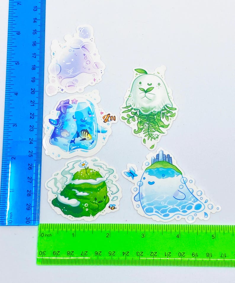 May include: A collection of five whimsical stickers featuring aquatic and natural themes. Designs include a jellyfish with fern-like tendrils, a floating island with a cityscape, and a sea creature with bubbles. The stickers are colorful and detailed.
