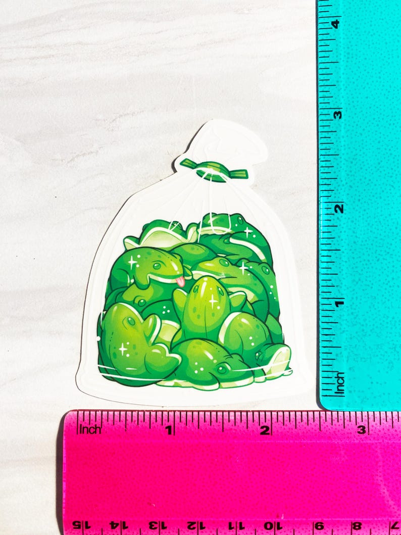 May include: A sticker featuring a clear bag filled with cartoon green frogs. The frogs have various poses, some with their tongues out. The sticker is approximately 3 inches tall and 2 inches wide.