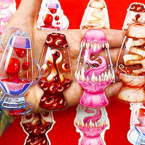 Puede incluir: Una colección de pegatinas transparentes únicas con diseños estilizados de lámparas de lava con varios elementos grotescos y surrealistas. Las pegatinas muestran colores vibrantes como el rojo, el rosa y el marrón, con detalles intrincados y un acabado brillante. Algunas pegatinas incluyen el texto "TYPE: O Negative".