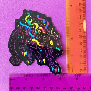 May include: A black and white sticker of a skeleton monster with neon colored details. The monster is surrounded by confetti and streamers. The sticker is approximately 3 inches tall.