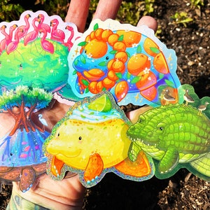 Könnte beinhalten: Fünf bunte, glitzernde Aufkleber mit Comic-Tieren. Die Aufkleber zeigen ein Seekuh mit Flamingos auf dem Rücken, ein Seekuh mit Orangen, ein Seekuh mit einer Limette, ein Seekuh mit einer Schildkrötenschale und ein Seekuh mit einem Krokodil auf dem Rücken.