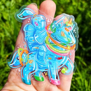 May include: A blue and rainbow unicorn sticker with a fish tail and a fish-shaped horn. The unicorn is wearing a series of colorful rings around its body and has a fish-shaped tail. The sticker is on a clear background.