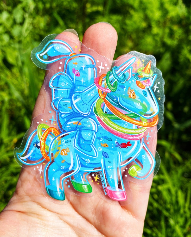 May include: A blue and rainbow unicorn sticker with a fish tail and a fish-shaped horn. The unicorn is wearing a series of colorful rings around its body and has a fish-shaped tail. The sticker is on a clear background.