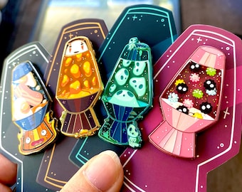 May include: Four colorful enamel pins shaped like lava lamps. Each lamp features a different design: a cartoon face, a ghost, a Totoro, and a Totoro with a flower.