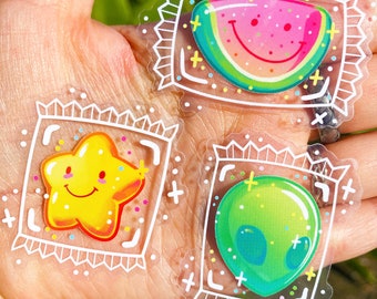 May include: Three clear stickers with white outlines and colorful illustrations inside. The stickers feature a smiling watermelon, a smiling star, and a green alien. Each sticker has a white border with a repeating pattern of plus signs and right angles.