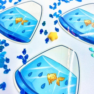 May include: A blue and white sticker with a goldfish in a bowl. The bowl is filled with blue water and has raindrops falling into it. The sticker is surrounded by blue fish confetti.