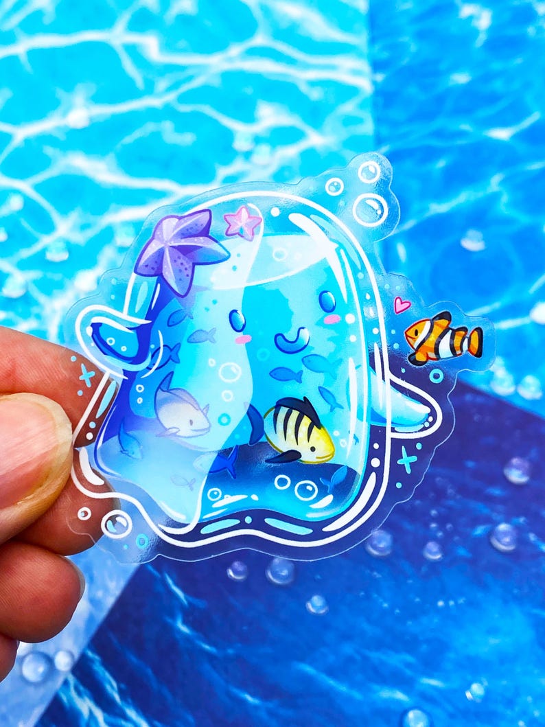 May include: A clear sticker featuring a cartoon jellyfish with a smiling face, surrounded by small fish, a starfish, and bubbles. The jellyfish is a light blue color, and the sticker has a white outline.