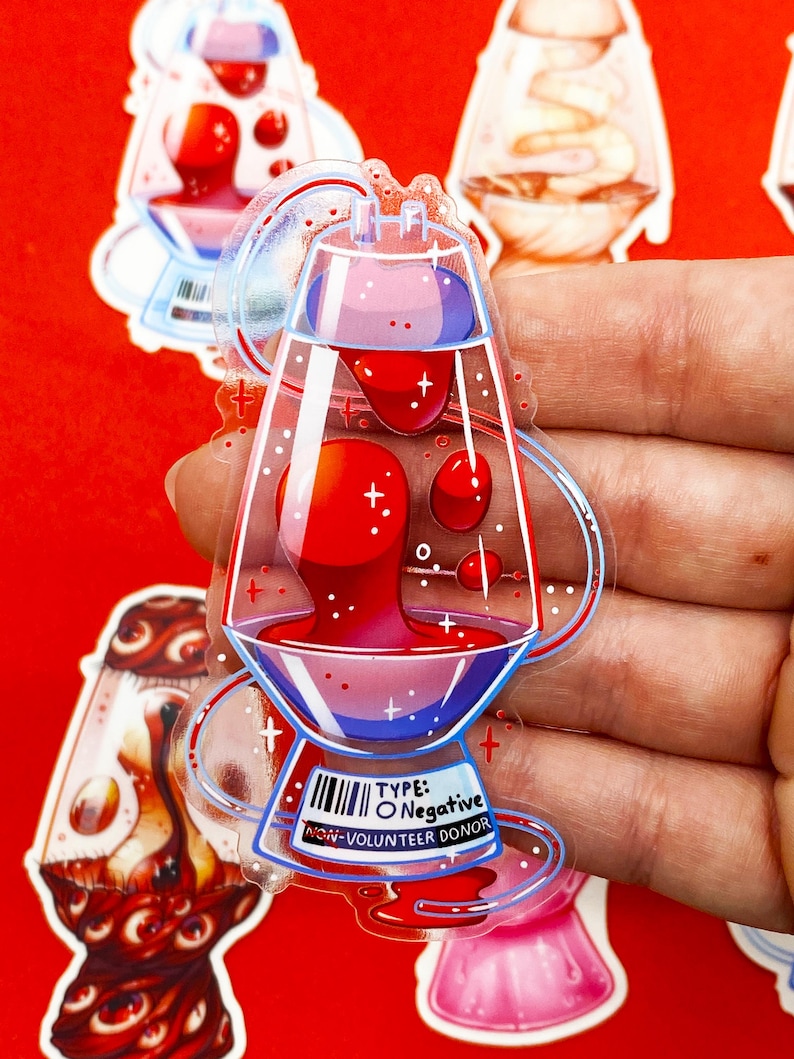 Pu&ograve; includere: Un adesivo trasparente con un design stilizzato di una lampada a lava con liquido rosso e viola. L'adesivo ha un codice a barre e il testo "TYPE: O Negative NON-VOLUNTEER DONOR". Sfondo rosso.
