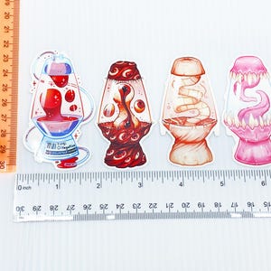 Pu&ograve; includere: Quattro adesivi unici con design di lampade a lava stilizzate. Il primo adesivo ha un liquido rosso con una base blu e testo. Il secondo ha un design rosso e marrone. Il terzo &egrave; arancione e bianco. Il quarto &egrave; rosa.