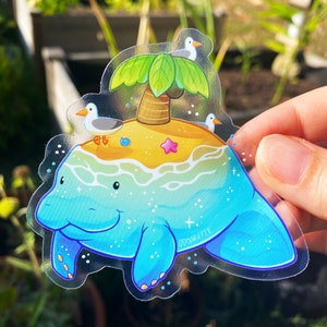 May include: A clear sticker featuring a cartoon manatee with a small island on its back. The island has a palm tree, a starfish, and three seagulls. The sticker has a blue, green, and yellow color scheme and the text "oddakettle" in the bottom right corner.