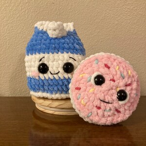 May include: Two crocheted plush toys, a blue and white milk carton and a pink donut with colorful sprinkles. Both toys have black eyes and smiling mouths.