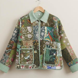 Pode incluir: Um casaco acolchoado com design de patchwork em vários tons de verde, castanho e padrões florais. O casaco tem gola, mangas compridas com punhos às riscas, fecho frontal com botões e dois bolsos quadrados grandes com debrum.
