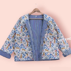 Könnte beinhalten: Eine blaue und weiße reversible Jacke mit einem floralen und tierischen Muster. Die Jacke hat einen Knopfverschluss und ein gestreiftes Futter.