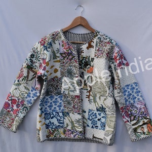 May include: A patchwork jacket with a floral and geometric pattern in shades of white, blue, pink, and green. The jacket is open-fronted and has long sleeves. The jacket is hanging on a wooden hanger.