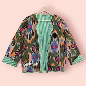 May include: A reversible quilted jacket with a green and white striped lining. The outer fabric features a colorful ikat pattern in shades of orange, blue, pink, and black. The jacket has a button closure and two patch pockets.