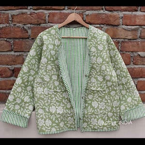 Könnte beinhalten: Eine grüne gesteppte Jacke mit Blumendruck und weißen Streifen. Die Jacke hat einen Knopfverschluss und eine lockere Passform.