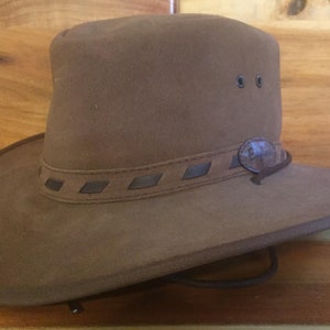 May include: A brown leather cowboy hat with a braided leather band and a small metal button on the side.