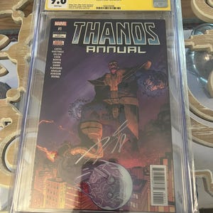 Puede incluir: Un cómic calificado que presenta a Thanos, un supervillano morado de Marvel Comics. El cómic se titula "Thanos Annual #1" y presenta una ilustración morada y negra de Thanos con un fondo morado. El cómic está calificado con 9.6 por CGC.