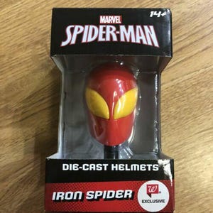 Könnte beinhalten: Roter und gelber Iron Spider Druckgusshelm, verpackt in einer schwarzen Box mit dem Marvel Spider-Man Logo. Die Box trägt auch den Text "DIE-CAST HELMETS" und "IRON SPIDER".