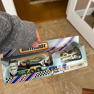 May include: Matchbox Team transport set with a green and white race car on a trailer and a white and yellow race car. The packaging is blue and white with the Matchbox logo.