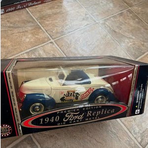 May include: A Premier Edition 1940 Ford Replica die-cast metal car in a display box. The car is cream-colored with blue fenders and features Pepsi-Cola branding. The box reads "1:18 Scale".