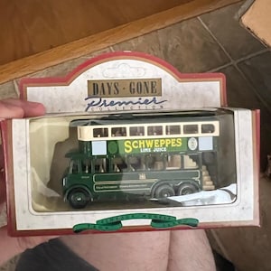 May include: A boxed Days Gone Premier Collection vintage model bus. The double-decker bus is green with white trim and features "Schweppes Lime Juice" branding. The packaging reads "Vintage Models From Lledo".