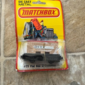 May include: A vintage Matchbox die-cast metal toy car on its original yellow and red packaging. The packaging features a picture of a truck and the text "#25 Flat Bed Woco". The toy is in a clear plastic case.