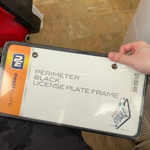 May include: A black license plate frame from Pro Elite. The frame is rectangular and has the words "PERIMETER BLACK LICENSE PLATE FRAME" printed on the packaging. The frame is in a clear plastic package.