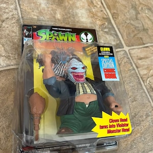 Peut inclure: Figurine d'action Spawn Clown en édition spéciale dans son emballage d'origine. La figurine est un clown avec un visage rouge et blanc, un pantalon vert et une veste noire. Le texte "Clown Head turns into Violator Monster Head" est inclus.