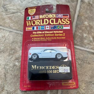 May include: A Matchbox World Class diecast model of a white Mercedes AMG 500 SEC. The car is in a red and black package with the Matchbox logo and text. The package includes the text "Collectors' Edition Series I".