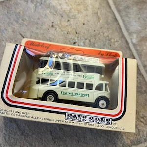 Puede incluir: Un autobús de dos pisos de color crema en miniatura, en su caja original. El autobús tiene ruedas negras y la inscripción "Festival Transport" en verde. La caja indica "Days Gone" y "Models of" con detalles de Liverpool.